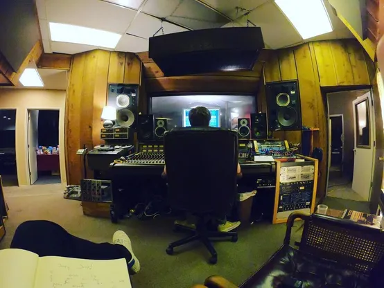 Picture of @plungepool from behind, sitting in front of a computer in the control room of a recording studio.