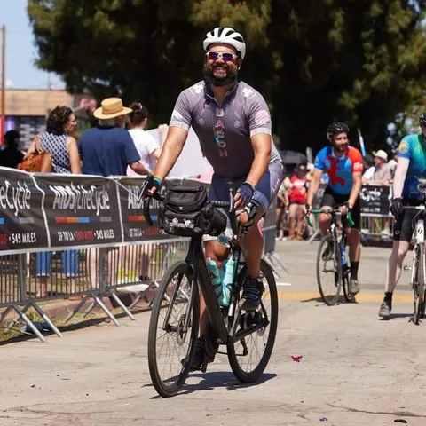 I am on my bicycle wearing a cycling kit that says BACON on the front, going through the finish line of the AIDS/Life Cycle in Los Angeles