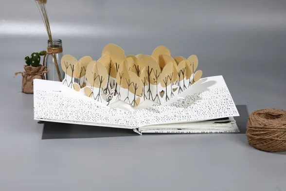 Una escena de un libro pop-up con un bosque de árboles de troncos negros y copas redondas amarillas. El libro está sobre un plató con objetos decorativos alrededor.

A pop-up book scene of a forest. The trees have black trunks and round yellow foilage. The book is photographed on a set surrounded by decorative props.