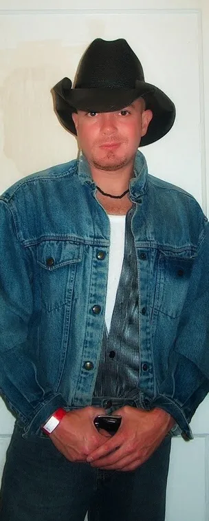 Man wearing a denim jacket and black cowboy hat.