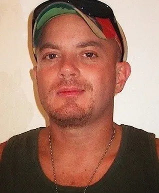 Man wearing a green t-shirt and flag hat, with sunglasses resting on the hat brim.