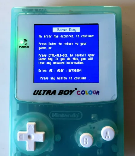 Photograph of a game boy showing a windows blue screen error, a qr code and the text: 
Game Boy
An error has occurred. To continue:
Press Enter to return to your game, or
Press CTRL+ALT+DEL to restart your Game Boy. If you do this, you will lose any unsaved information
Error:
Press any button to continue _