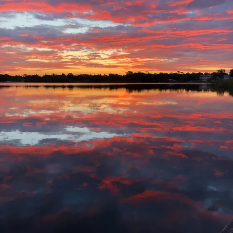 An especially vibrant pre-sunrise dawn on a lake with beautiful shades of red, orange, yellow, and blue in the clouds, reflected in the water.