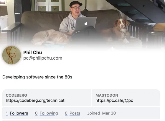 fediverse profile showing me working on a laptop on a sofa with a dog on each side