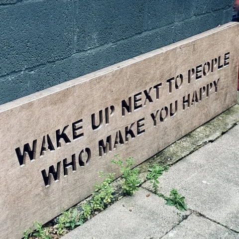 A wooden sign with the text
WAKE UP NEXT TO PEOPLE
WHO MAKE YOU HAPPY