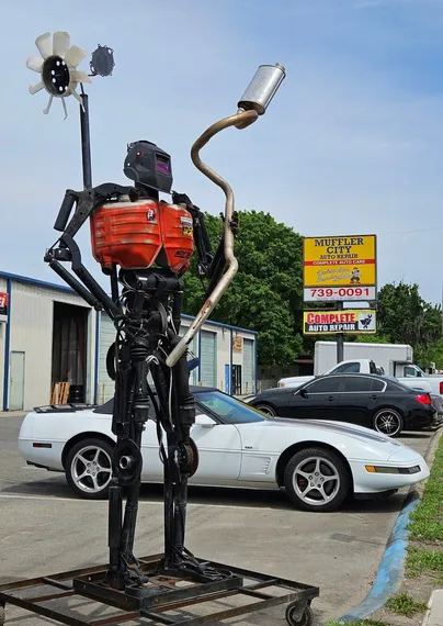 Iron-man type figure made from mufflers and auto parts stands guard in front of an auto repair shop.