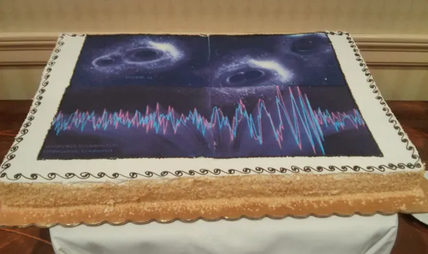 A cake celebrating the first observation of gravitational waves. The cake shows an artistic representation of a binary black hole coalescence as well as the data for GW150914 from the Advanced LIGO detectors