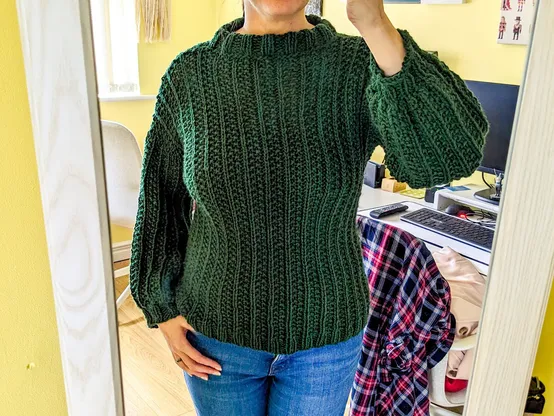 Reflection of my torso as I model a very recently completed, but not blocked yet, knitted jumper. It's forest green, and made up of a squishy broken rib stitch pattern.