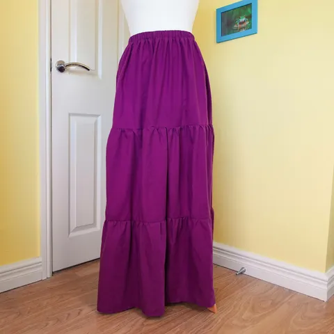 Three-tiered purple skirt displayed on a dressmaking dummy, in a room with yellow walls. Each tier is more gathered than the last, and the waistband is elasticated. This skirt was made from a £2.50 bed sheet!