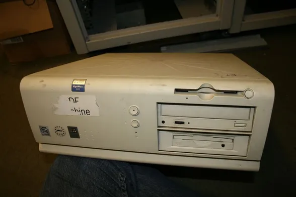 photo of an old battered desktop computer. It looks grimey, has a floppy disk and CD drive, and a peeled off sticker on it