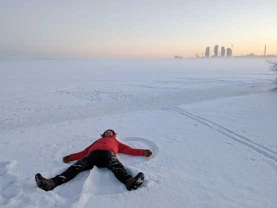 Me on my back in the snow, making a snow angel. In the distance the tall buildings of the Kalasatama region in Helsinki can be seen.