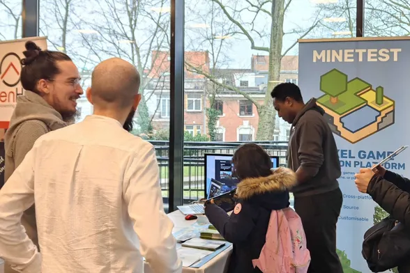 A girl playing Minetest on a steam deck. A table with leaflets and a laptop. A large roller banner saying "Minetest - voxel game creation platform"