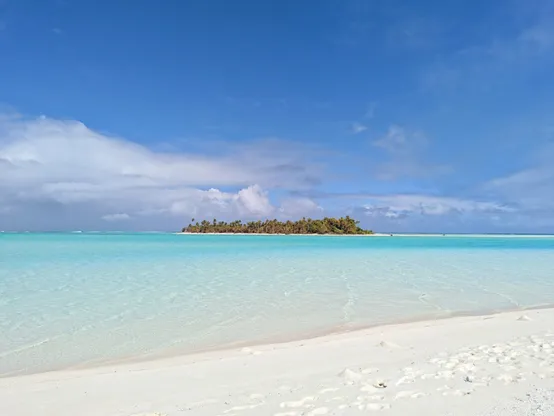 View from a white sand beach on a palm tree covered island in turquoise water in the Aitutaki Lagoon in the Cook Islands in the South Pacific Ocean.