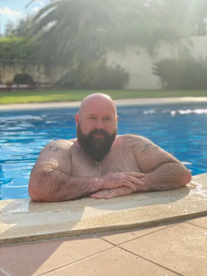 Image shows Rob leaning on the side of swimming pool. 