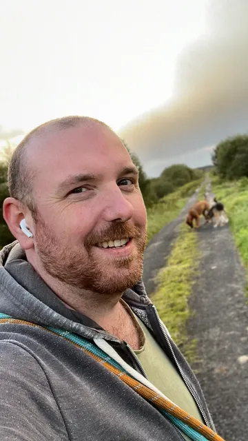 A selfie showing me from the chest up, walking on a country lane with our dogs in the background.