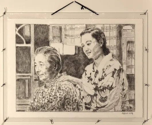 A framed black and white pencil drawing of two Japanese women, one elderly (Tomi) and one younger (Noriko), in a rather dark room with a bright square of light coming through a partly-obscured window. They both wear light-coloured yukata, Tomi's in a conservative pattern of small blossoms, Noriko's in a bold pattern of large dark thistle-like flowers. Noriko s rubbing Tomi's shoulder and smiling faintly.