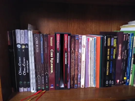 A shelve full of RPG books and modules including D&D's Rules Cyclopedia and other old material, OSR stuff, the 3E and 5E D&D rulesets, GURPS, The Dark Eye, the Shadows of Esteren, Pathfinder, Stormbringer, the Call of Cthulhu RPG and more.