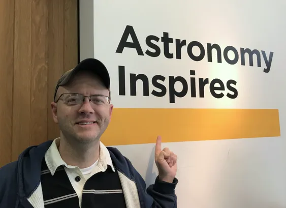 Photo of a the author pointing at a sign that reads "Astronomy Inspires"