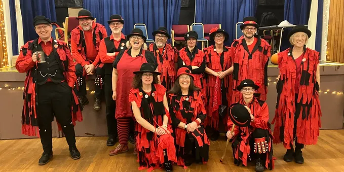 A group of morris dancers all in red and black, almost all wearing tatter jackets. Lots of smiles, and hopefully a sense of fun - that is certainly what we aim for.