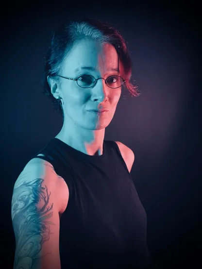 Selfie in front of a black backdrop, wearing a black sleeveless top,  with a blue key light from the left and a orange fill/edge light from the right