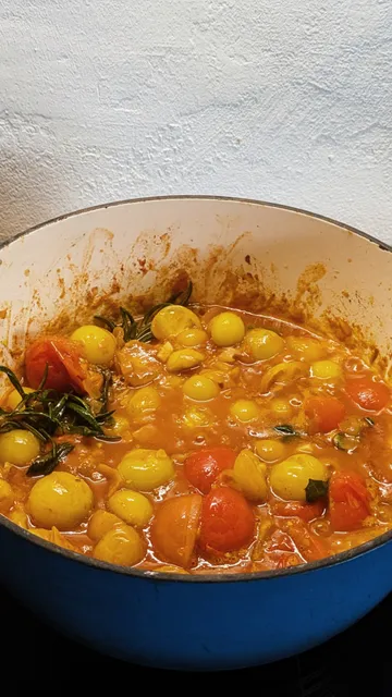 In einem blauen Emaille-Topf kochen allerlei Tomaten und Gewürze.