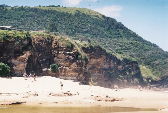 A photo of some people on a beach, a hill behind where people are hang-gliding. Shot with a Ricoh KR-10 Super on Fujifilm  C200.