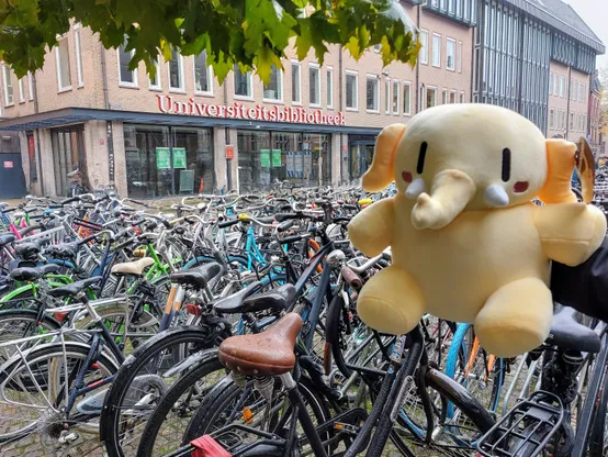 Plushtodon in front of the University of Groningen Library building, lots of bikes in the background