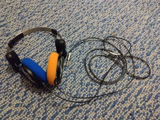 a picture of black koss porta pro headphones with blue and orange earpads and an nice, braided cable with some aluminium connectors and bits on a white/blue carpet.
