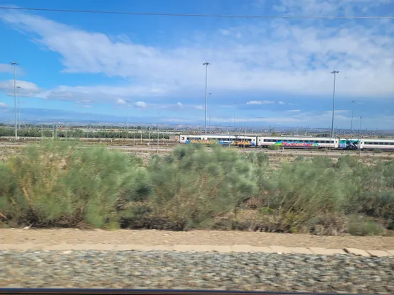 Train depot west of Zaragoza. Green bushes along the railway. A few high altitude clouds.