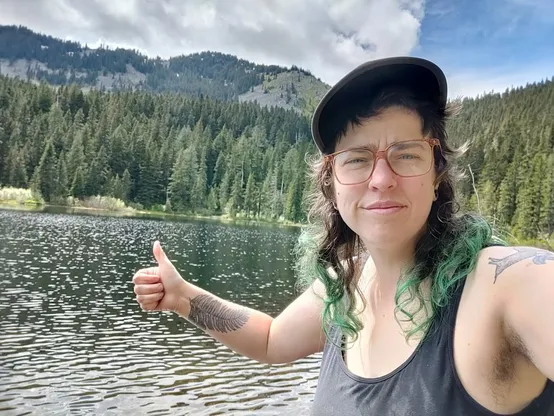 Karen standing in front of an alpine like, extending their thumb upward in approval. 