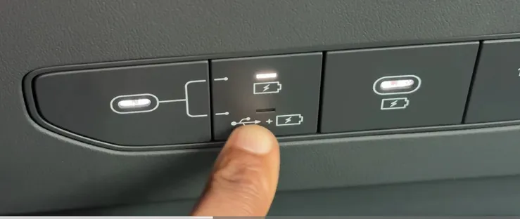 A photo of a YouTuber’s finger pointing at a button on the new Kia EV9 that shows two modes next to a USB port.  The symbols indicate two choices:  Battery only, or battery with USB data.