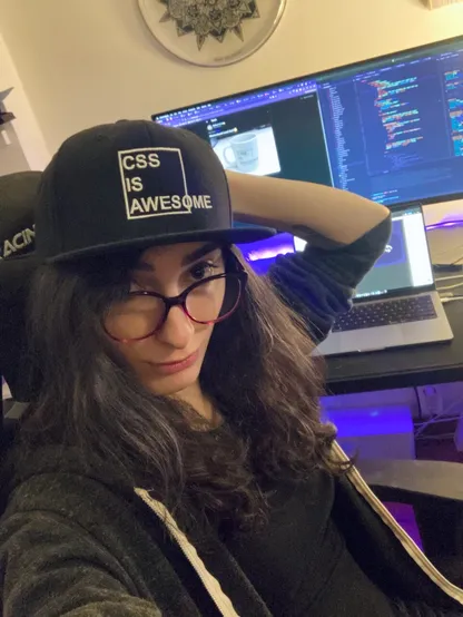 selfie in front of my previous desk, wearing a "CSS IS AWESOME" cap