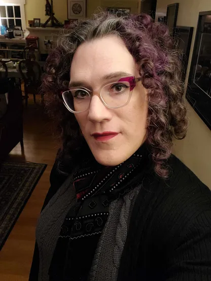 Photo of your author looking up at the camera. She's wearing a rich burgundy scarf and her trademark purple-cornered glasses, with purple curly hair cascading down to her shoulders.