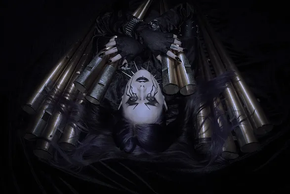 a photo of me lying on the floor. i have corpse paint makeup that looks like dramatic tears. in my arms i'm holding a bunch of organ pipes with my hair strewn across them.