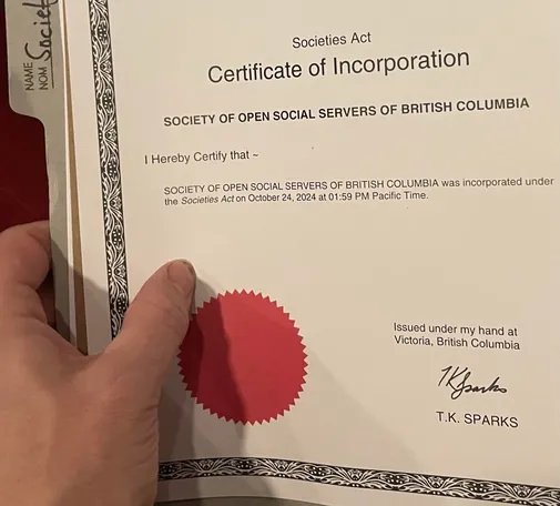 A close-up as I hold one side of a file folder, which contains on the top a certificate of incorporation for the society. It includes a red seal.