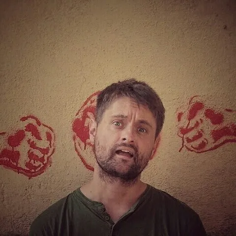 A man acting as he's about to be crushed by a couple of fists painted on a wall behind him