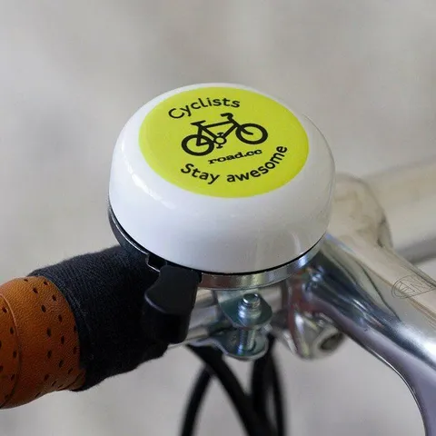 A close up of a bicycle bell attached to a handlebar. In the centre of the bell is a line drawing of a bicycle and around the edge it says, ‘Cyclists stay awesome’.