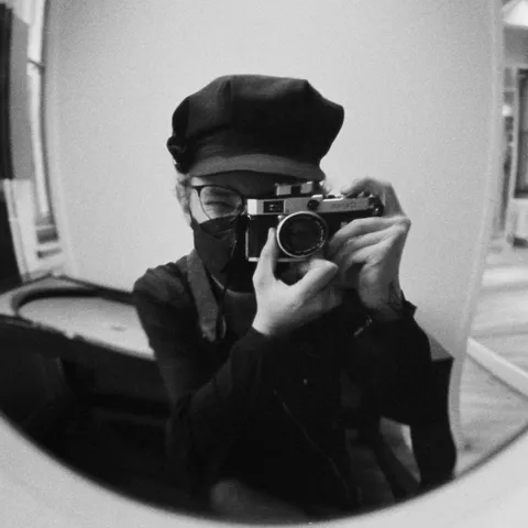 B/W photo in a mirror of myself looking through a Canon P rangefinder camera. I'm wearing a black balloon cap and jacket and a black face mask.

The convex mirror distorts the view into a very wide-angle