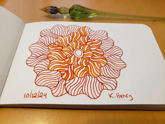 Hand drawn generative/procedural art in ink on an open page of my sketchbook. The abstract pattern is floral. My glass dipping pen is next to my sketchbook.
