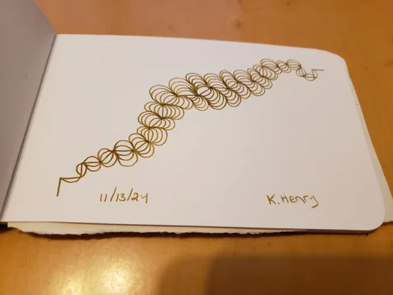 Hand drawn generative art in ink on an open page of my sketchbook. The abstract pattern looks like it could be a broken hair scrunchi, or a strange worm that is fat in the middle.