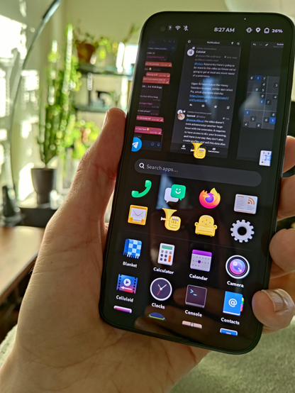 Photo of a hand in a sunny living room, holding a phone. The phone sports the Gnome mobile app launcher and some multitasking cards.