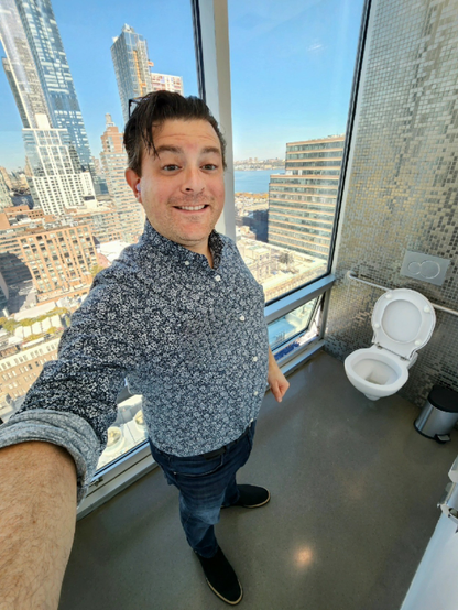 Jerry Levine standing next to a toilet that's in front of a sheer glass window