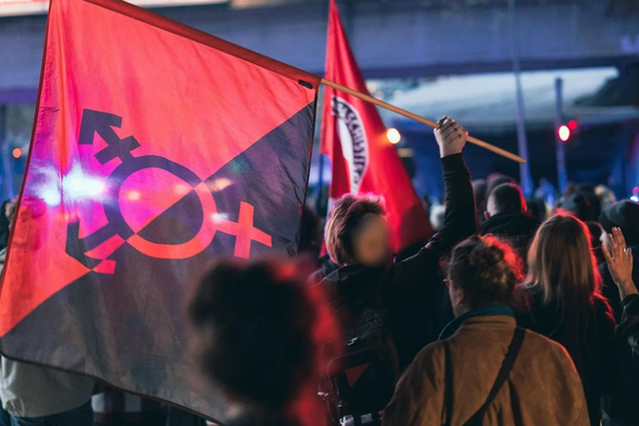 Me hoisting an anarcho-transgender flag at an antifa march.  I'm sporting a pink deathhawk and the three arrows I have tattooed on my right hand are visible. 