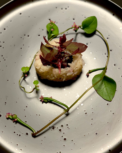 On a black speckled plate reflecting light so that it appears grey is a delicate bowed frond of malabar spinach with pink dainty blossoms on tubular fronds. In the center of the verdant spiral is a dyed faintly pink roll, with dyed rice inverted to the outside.
Inside the roll is soy pickled mizuna stems. On top of the roll is a flowering frond of red Hopi amaranth. So serene! 