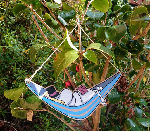 A photograph of a small tree, with an illustration of a snoozing moomin pappa in a hammock hanging from it. It is hanging with real string, but the hammock and moomin pappa are drawn on card.