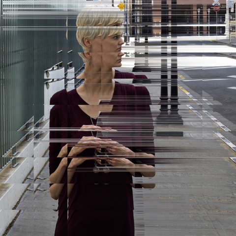 Woman with short blonde hair on street looking to the side, with photo pixelsorted to create elongated look.