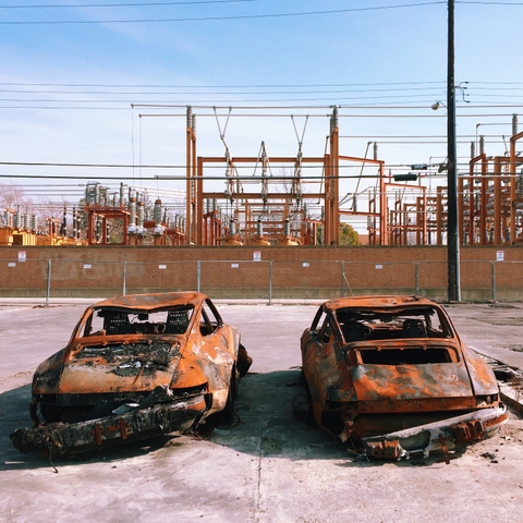 Two rusted and fire-damaged porches side-by-side, facing a wall with electric grid infrastructure behind.