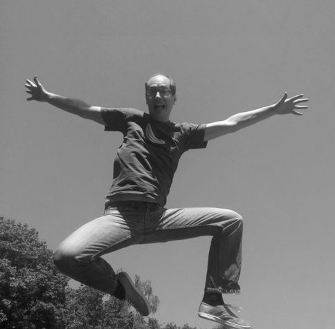 Black-and-white image of me jumping in the air, arms stretched and looking slightly terrified because I planned the jump better than the landing.