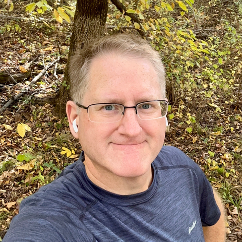 Selfie in the woods of a Caucasian man wearing a blue shirt and glasses. 