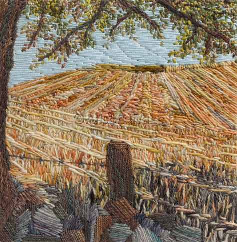 Stitched artwork depicting a harvested wheatfield with stripes where the combine has mown. A tree in the forground to the left overhangs a stone wall and barbed wire fence